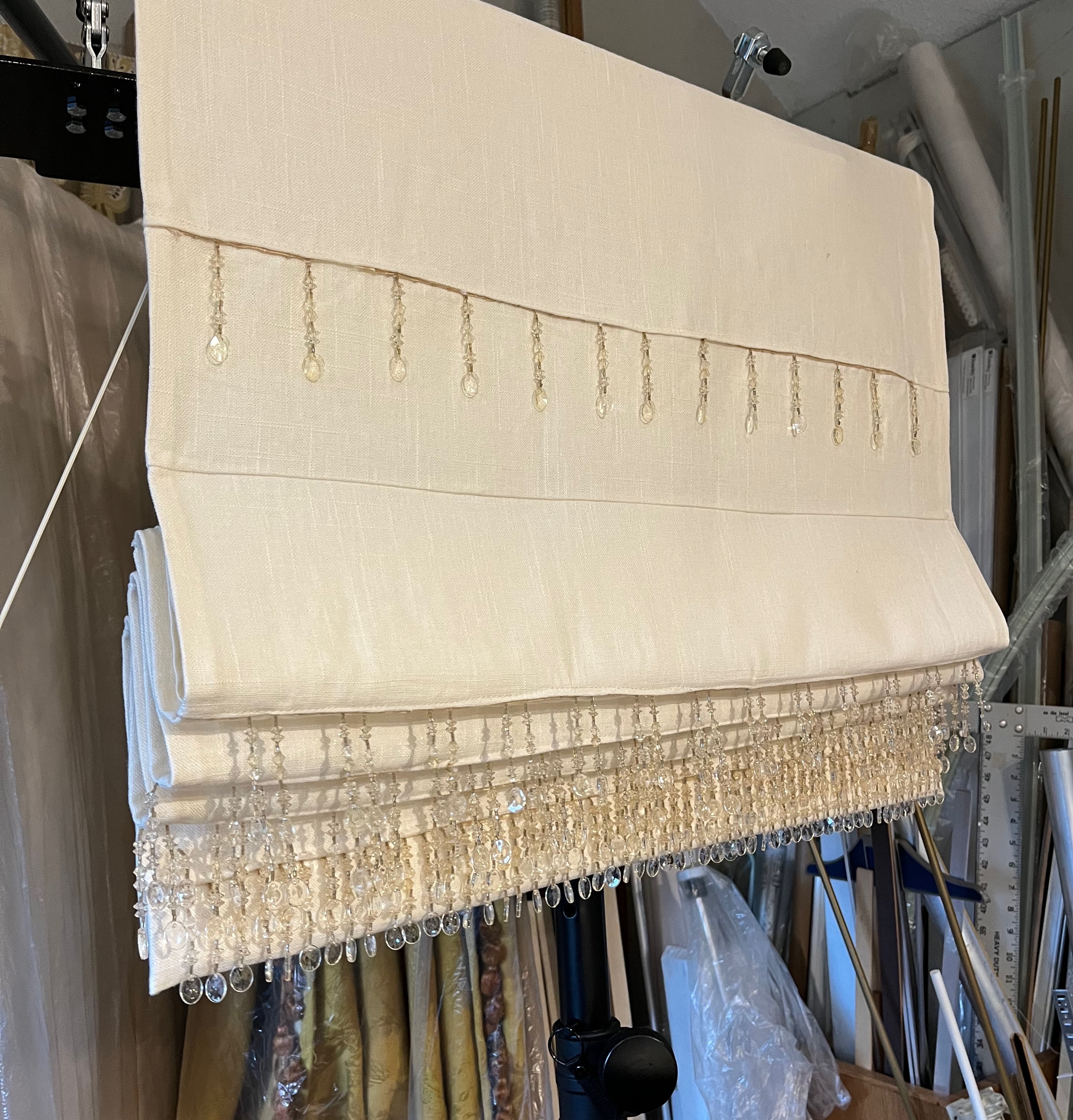 Cream roman shade with crystal and gold beaded trim in workroom