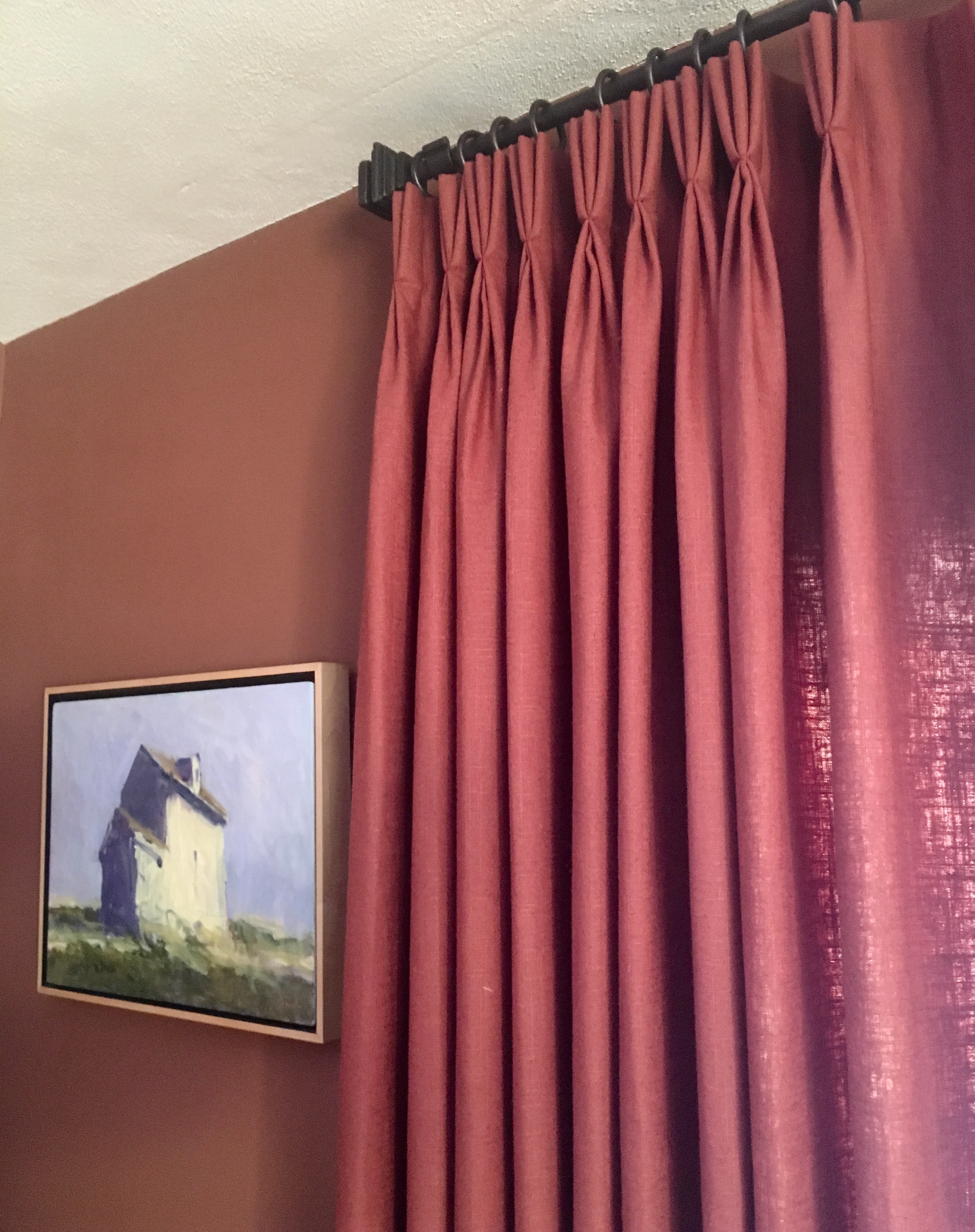 Red linen pinch pleat drapes on dark rod against terracotta wall